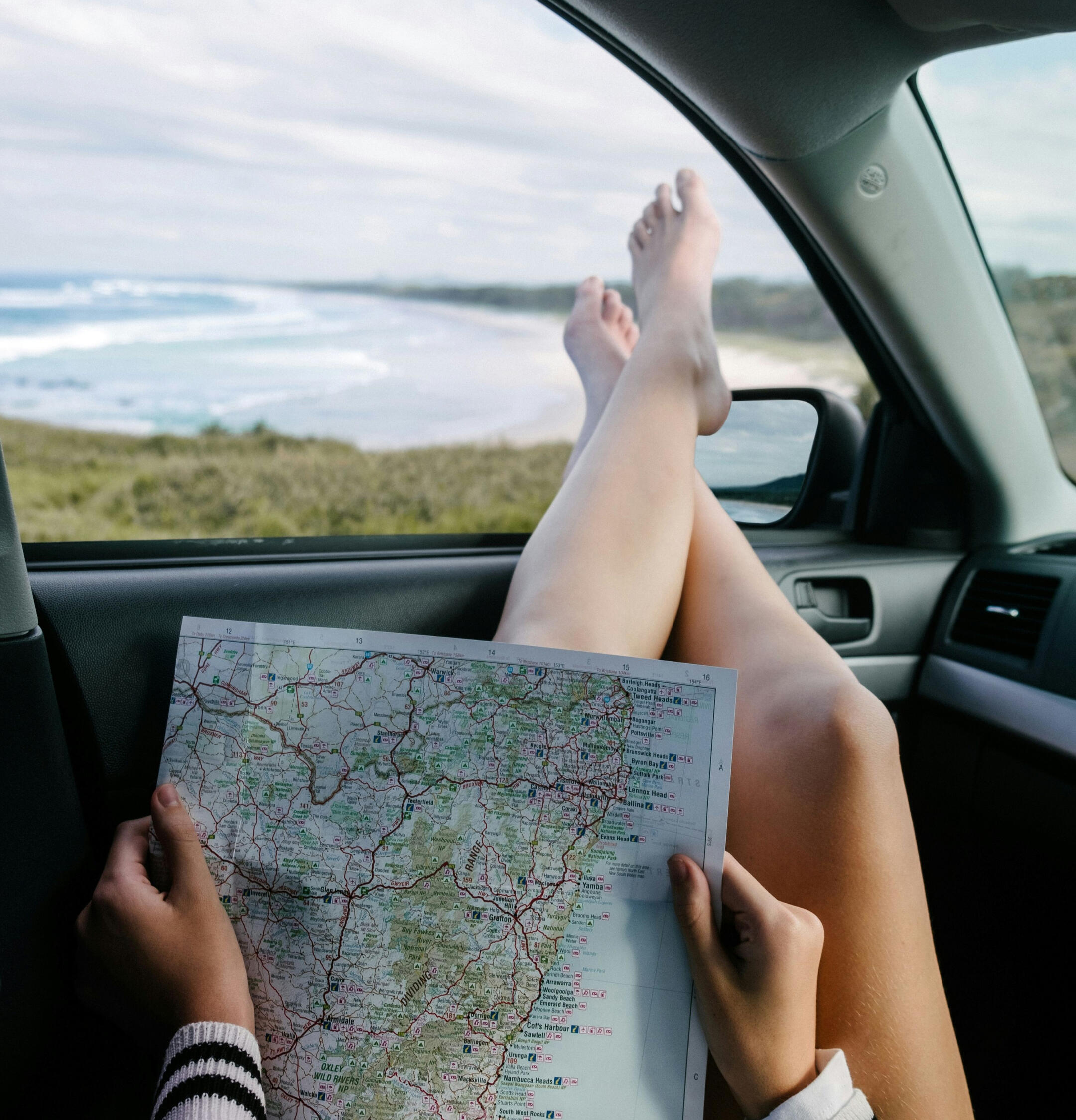 Woman map Gold Coast A lady sitting with her legs out the window looking at a map of east coast Australia with the beach and coast line visible out the window